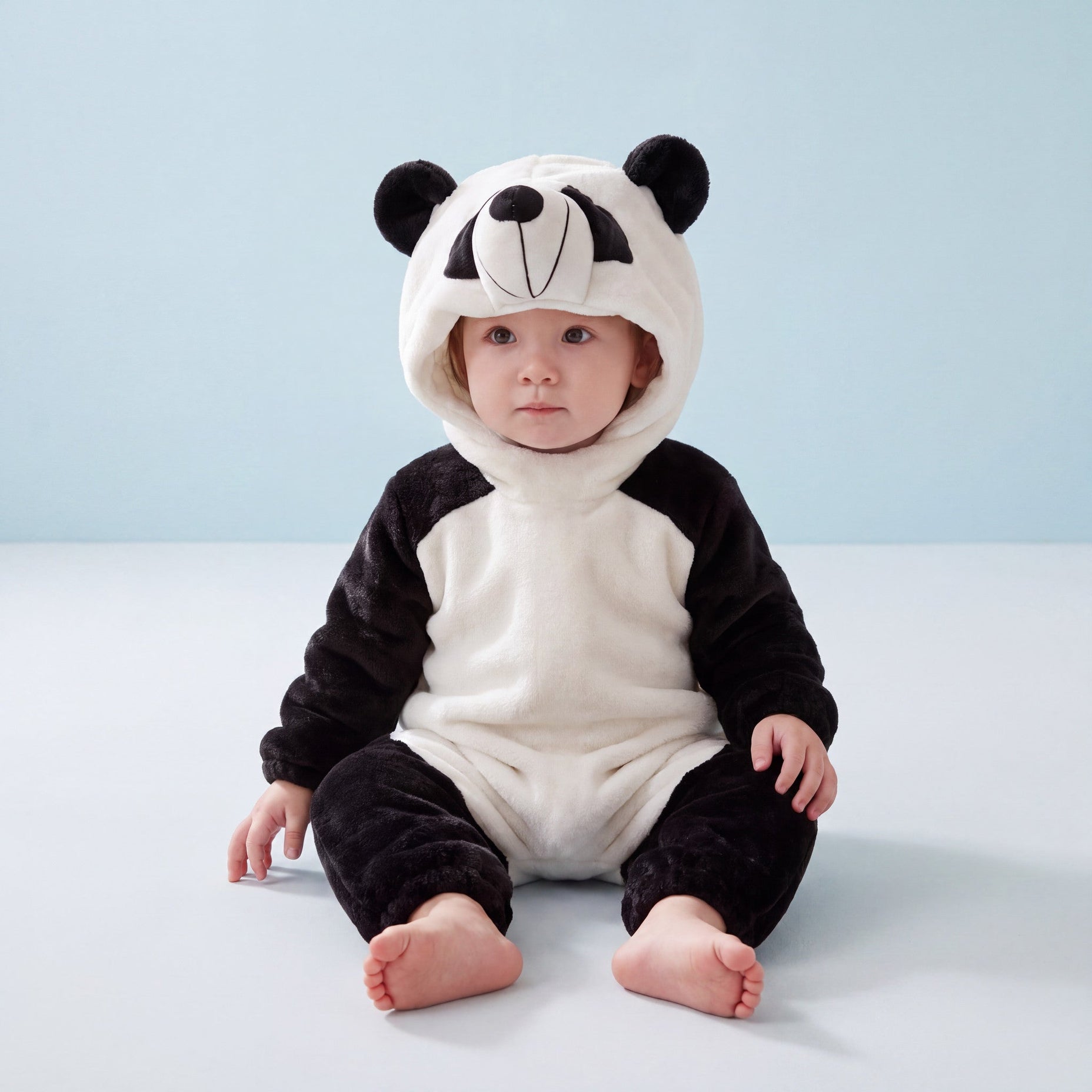 Panda one-piece on child in a high-angle view against a pale-blue background, attached panda hood and open ankle cuffs.