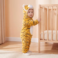 Select Tiger one-piece on child in a supported standing pose in a peach nursery, attached tiger hood and pale lower-foot sections.